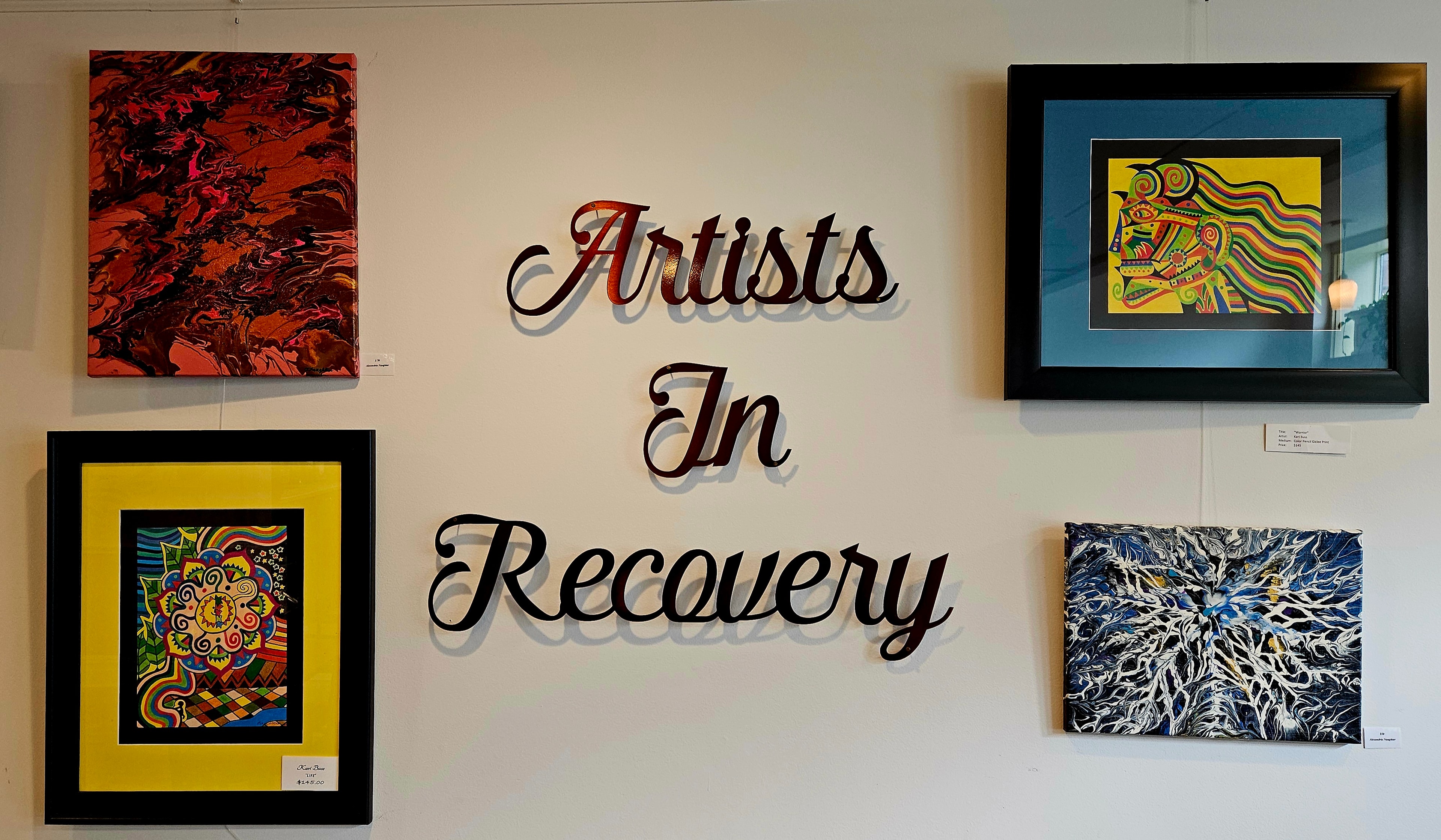 Artists In Recovery gallery wall with four framed paintings at Café The Lodge